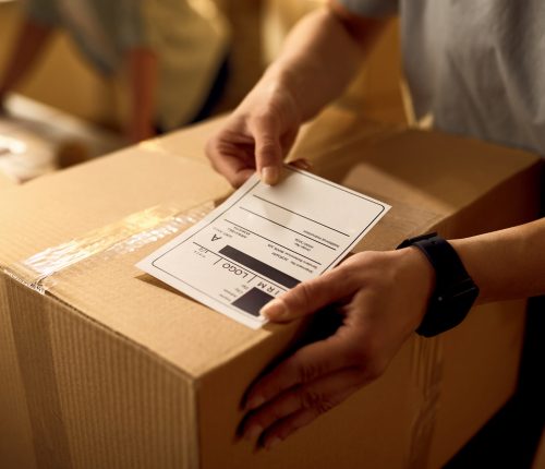 Close-up of courier attaching address label on a package while working in the office.